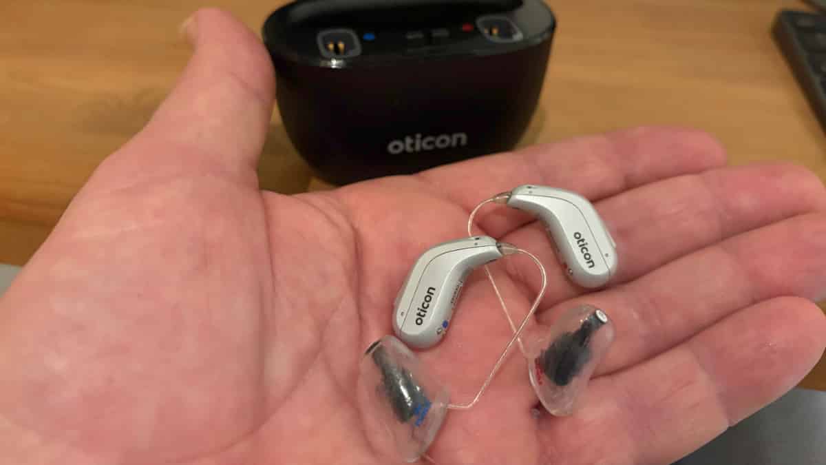 Photo of my Oticon Reveal hearing aids with custom earmolds for my severe-to-profound hearing loss, with the charger in the background.